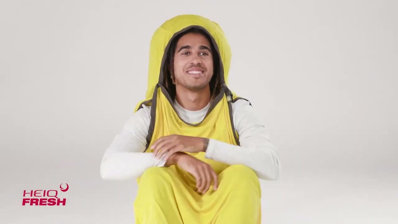 male model wearing a yellow sleeping bag liner, with the hood on, making a goofy silly smile