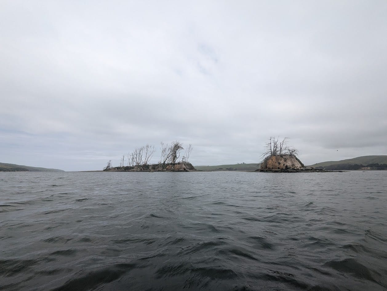 two small, seemingly uninhabited islands with a few scrubby trees. cloudy skies and waves