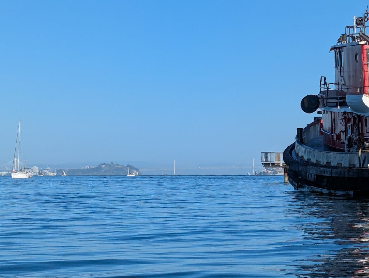 a big tugboat, and the san francisco bay bridge in the distance