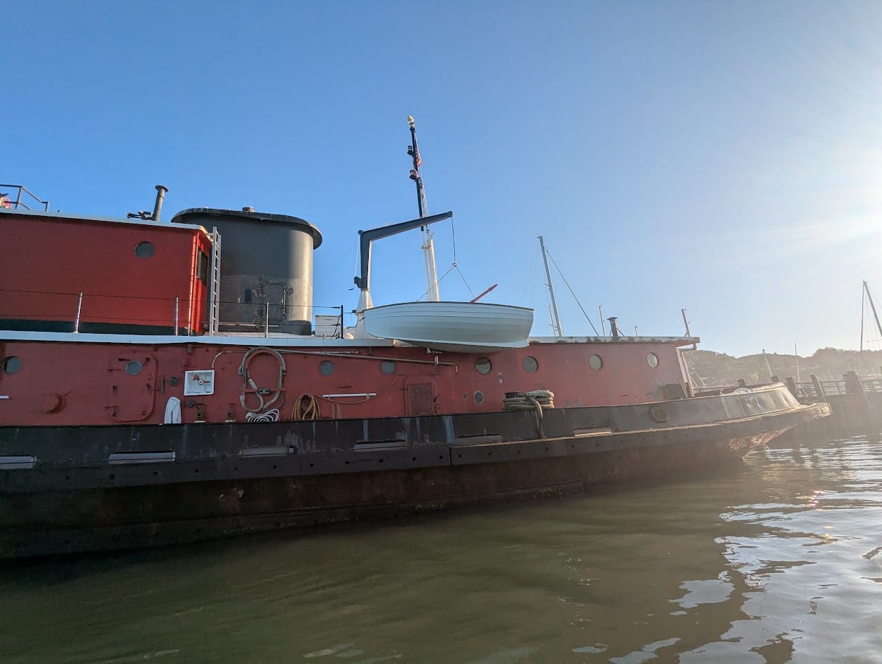 a tugboat with a crane holding a cute little wooden rowboat