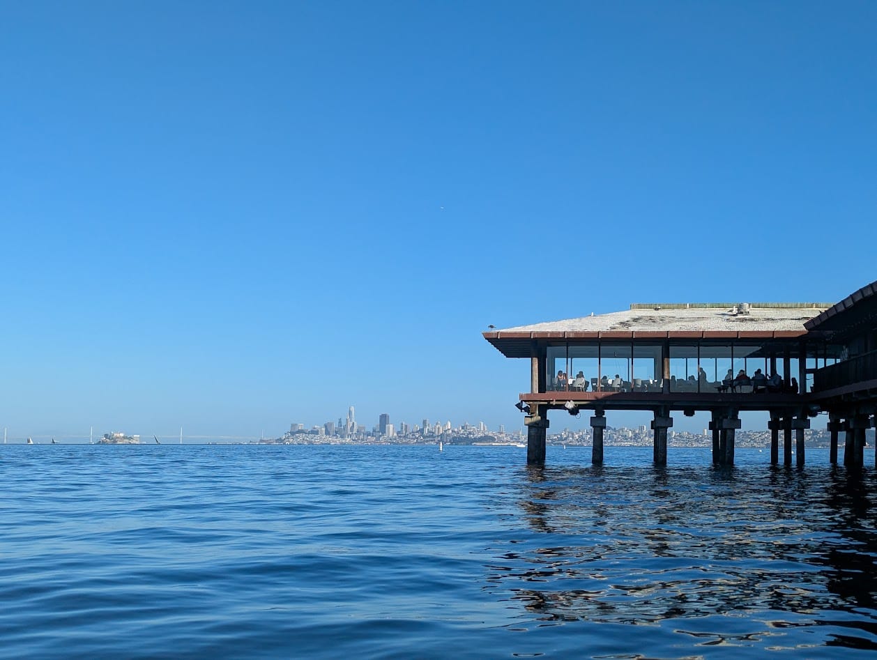 waterfront dining room out over the water on piers, with the san francisco skyline in the background