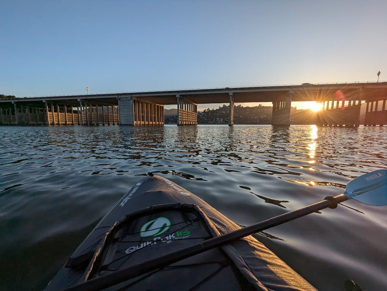 paddling towards a bridge at sunset