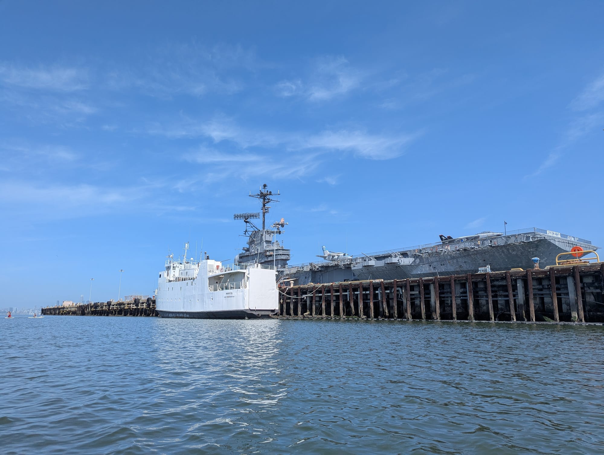 an old white boat, parked across from the much larger USS Hornet. you can see planes on the deck of the hornet.