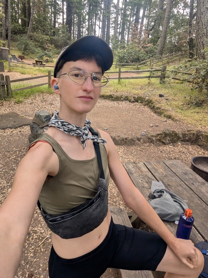 me at a picnic table at a campground, all geared up for a big hike, looking clean and not sweaty yet