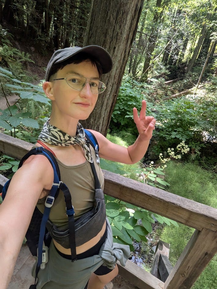 me on a footbridge in the forest holding up 2 fingers