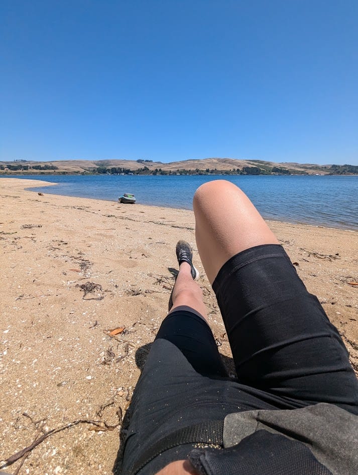 my legs lounging on a beach, with my boat in the background. no one else is on the beach or anywhere else in sight
