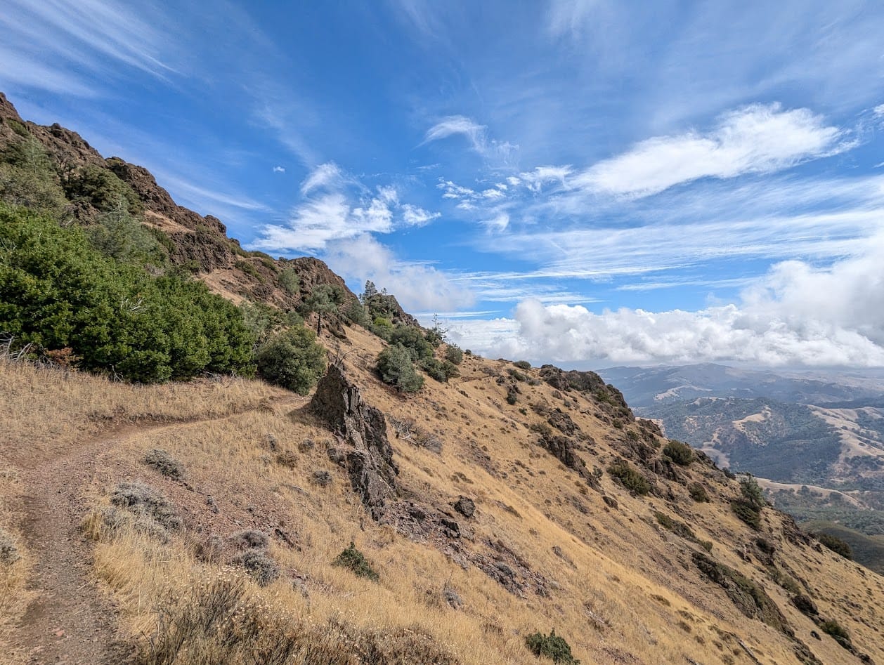 trail on the side of a steepish hill, beautiful sky with clouds, and a view over mountains